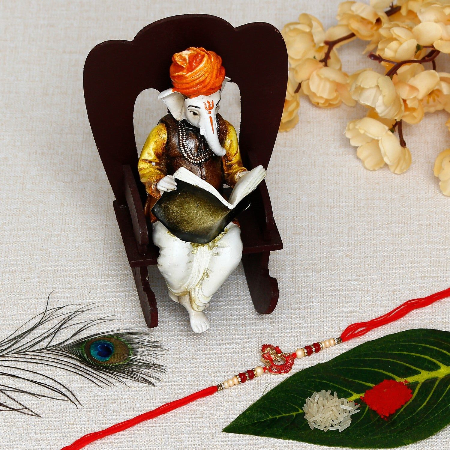 Designer Ganesha Rakhi with Lord Ganesha reading Book on Wooden Chair and Roli Chawal Pack