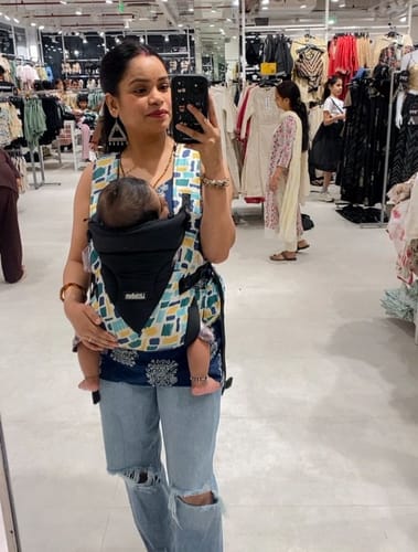 New mom holding her baby in a shopping mall promoting Beepops protein bars as a quick on-the-go snack for busy mothers